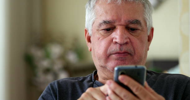 Frustrated senior using cellphone device at home. Upset older person looking at smartphone stock photo