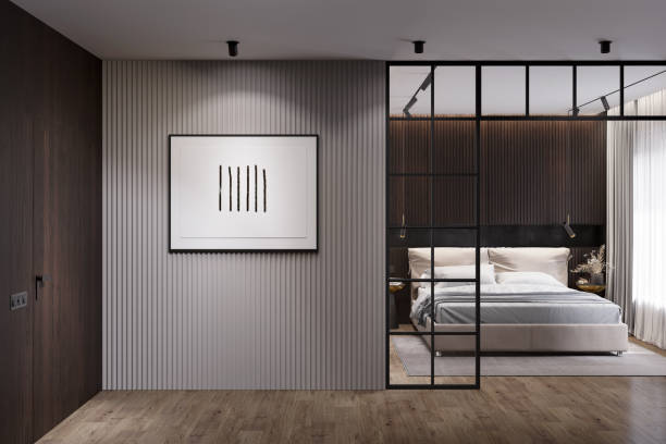 appartement moderne sombre avec une affiche horizontale éclairée sur un mur gris entre une porte en bois et une cloison en métal, une chambre avec un lit beige près de la fenêtre en arrière-plan. vue de face. - spot lit photos et images de collection