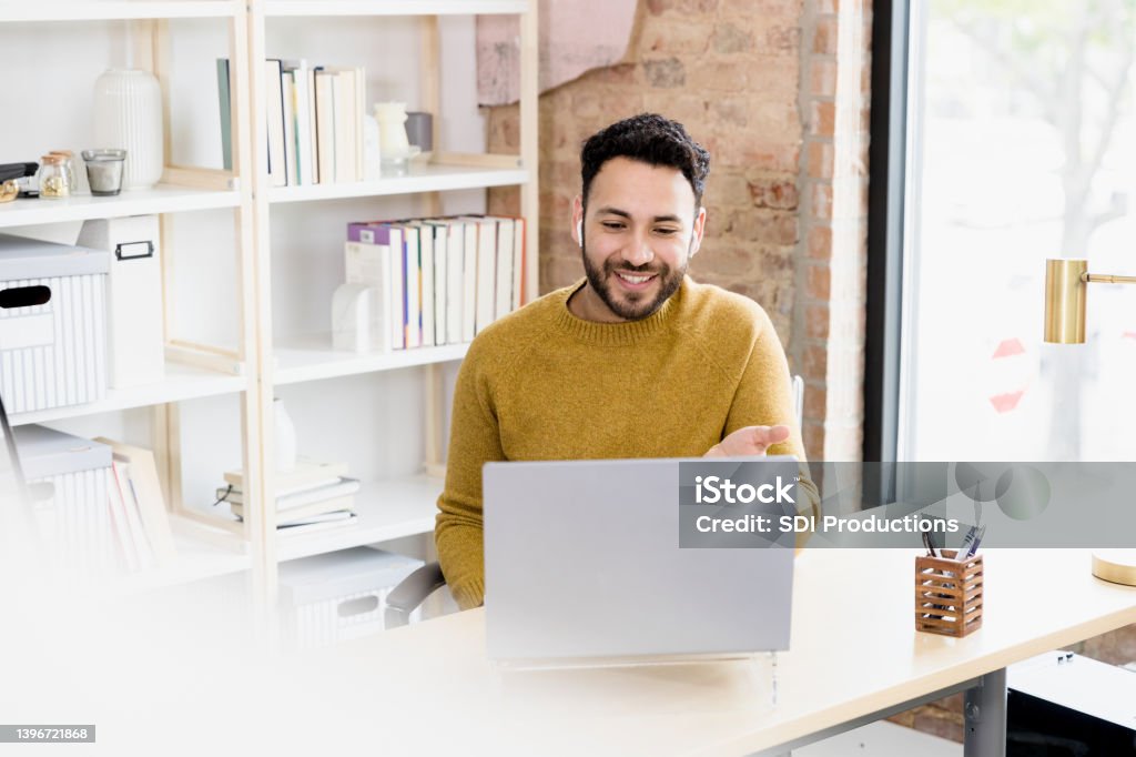 Man uses laptop to video conference with friends The young adult man uses his laptop to video conference with friends. Men Stock Photo