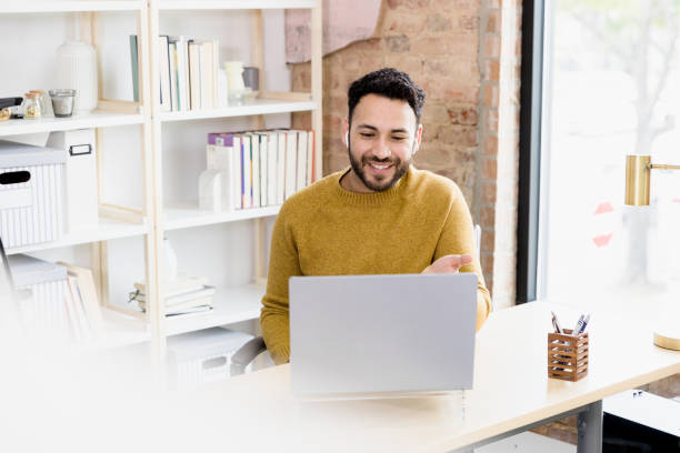 Man uses laptop to video conference with friends The young adult man uses his laptop to video conference with friends. hispanic guy stock pictures, royalty-free photos & images