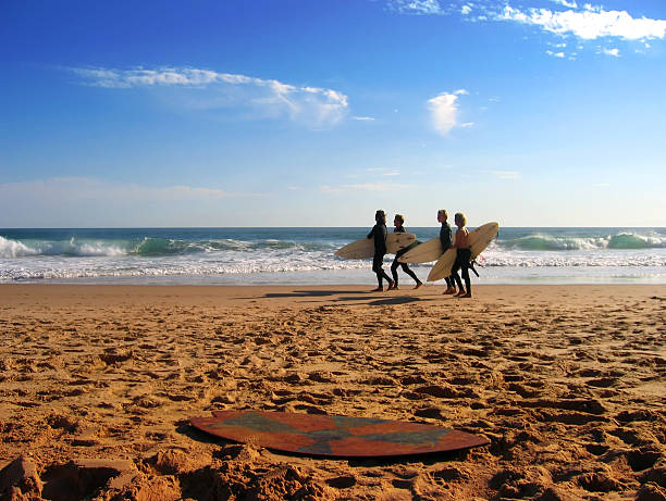 A distant shot of friends going surfing at the beach Surfers walking along the beach at Cape Woolamai, Victoria, Australia. downunder stock pictures, royalty-free photos & images