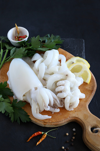 Two fresh squids with lemon and herbs prepared for cooking on dark background. Fresh seafood. Directly above.