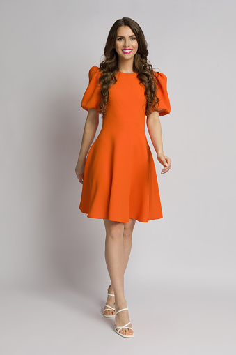 Beautiful smiling young woman in orange cocktail mini dress with puffed short sleeves and high heels. Full length studio shot on white backgound.