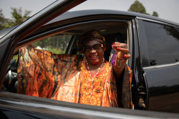 eine afrikanische dame, die in ihrem auto sitzt, hält schlüssel in der hand, konzept der autovermietung. - car old african descent car salesperson stock-fotos und bilder