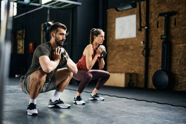 coppia atletica che fa esercizio di squat a calice kettlebell durante l'allenamento incrociato in palestra. - kettle bell sport women muscular build foto e immagini stock