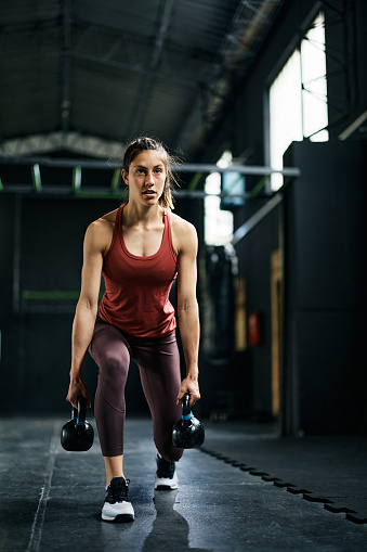 Athletic woman doing kettlebell walking lunges during sports training  in health club.