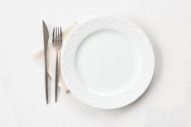 istock Empty white plate with fabric napkin, a fork and a knife on white table. Top view. 1396728065