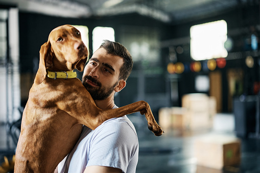 Male athlete holding his dog while having sports training in a gym.