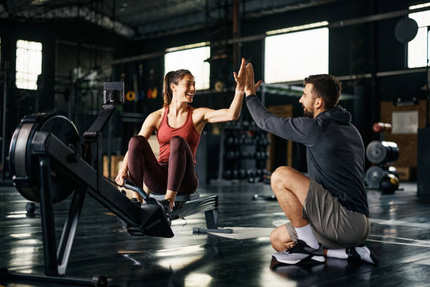 Happy athlete giving high-five to her personal trainer after exercising on rowing machine in a gym. Supportive fitness instructor giving high-five to athletic woman after exercising on rowing machine during cross training in a gym. fitness instructor stock pictures, royalty-free photos & images