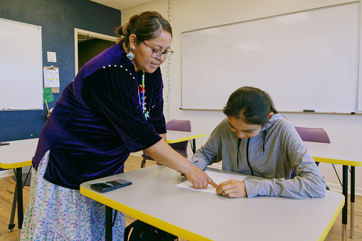 An Indigenous Navajo high school teacher with a group of students in a school classroom.