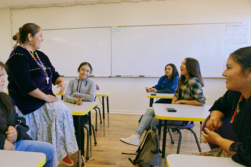 An Indigenous Navajo high school teacher with a group of students in a school classroom.