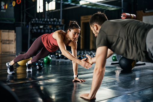 Young gym partners doing clap push-ups while having sports training in a gym.