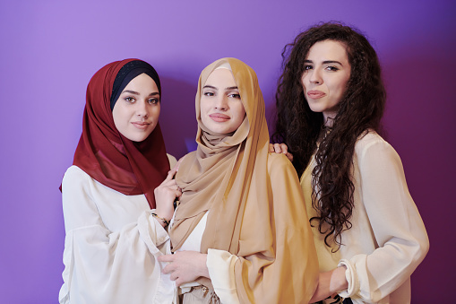 group portrait of beautiful muslim women two of them in fashionable dress with hijab isolated on purple background representing modern islam fashion and ramadan kareem concept