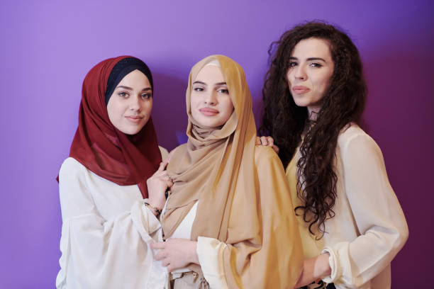 muslim women in fashionable dress isolated on purple group portrait of beautiful muslim women two of them in fashionable dress with hijab isolated on purple background representing modern islam fashion and ramadan kareem concept arabian girl stock pictures, royalty-free photos & images