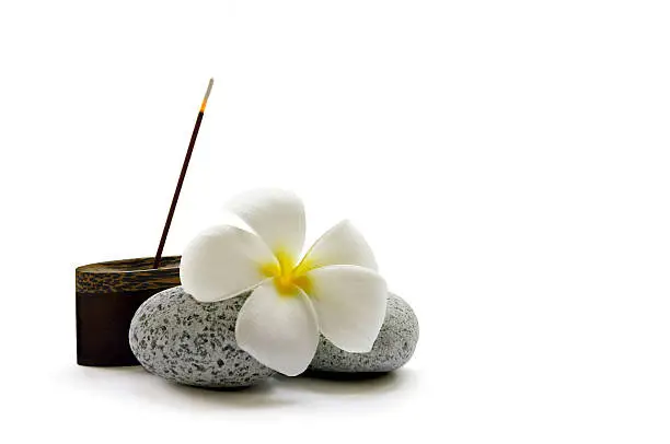 A stick of fragrant Japanese incense, some smooth pebbles and a frangipani flower