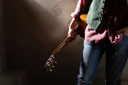 Man holding acoustic guitar. Musician in studio with classic acoustic guitar near wall