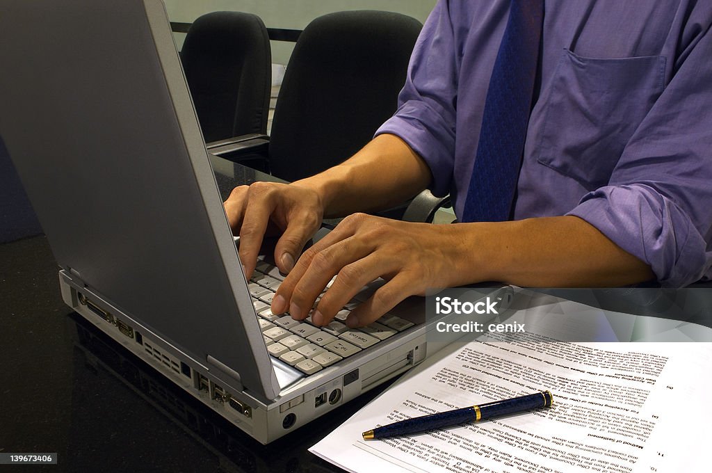 Typing On The Computer Close-up of a man's hands typing on the computer in the office with some documents, blank paper and pen next to him Minute Hand Stock Photo