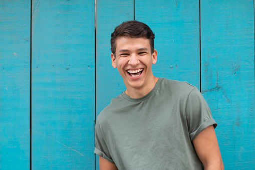 Young latin with an authentic laugh, in the background a blue door typical of latin homes. Latin representation in a portrait.