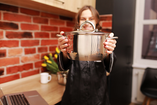 Online cooking tutorial. cropped photo hand of woman girl using laptop for vlogging blogging holding saucepan in the modern kitchen.