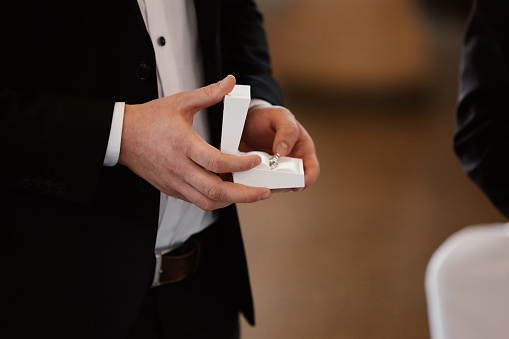 The groom holds gold wedding rings in a white box for the bride in the morning on the wedding day