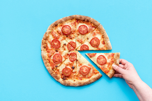 Woman's hand taking a slice of pizza. Above view with a homemade vegetarian pizza on a blue table.