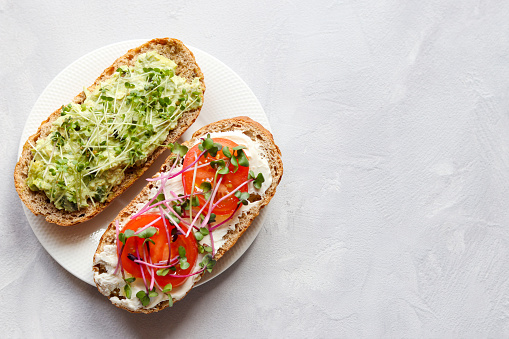 Two toasts with avocado, tomatoes and microgreens. Healthy food. Tasty homemade appetizer, or breakfast. Top view with copy space.