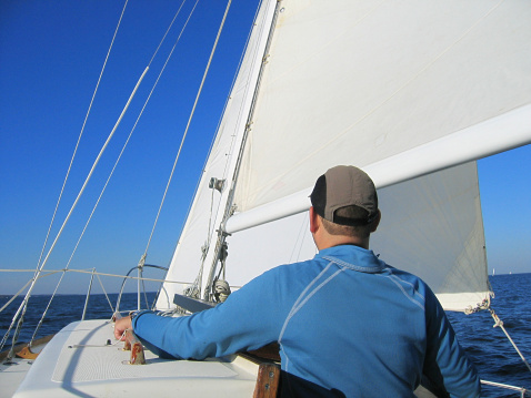 Person steering a sailboat.Focus on Sails.  Beutiful fall day with blue skies and great breeze.