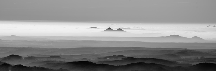 Bezdez twin mountains rising from the mist. Weather temperature inversion, Czech Republic. Black and white image.