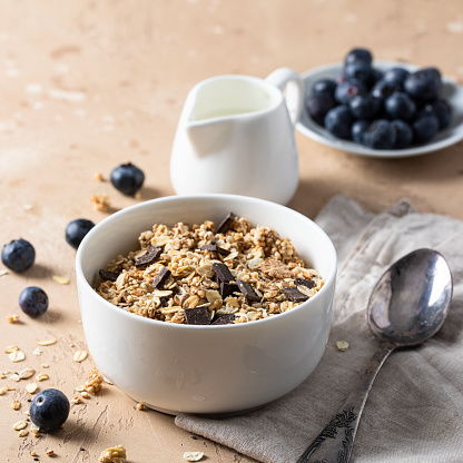 Muesli with chocolate in white bowl served with blueberry and milk on the table . Healthy breakfast concept.