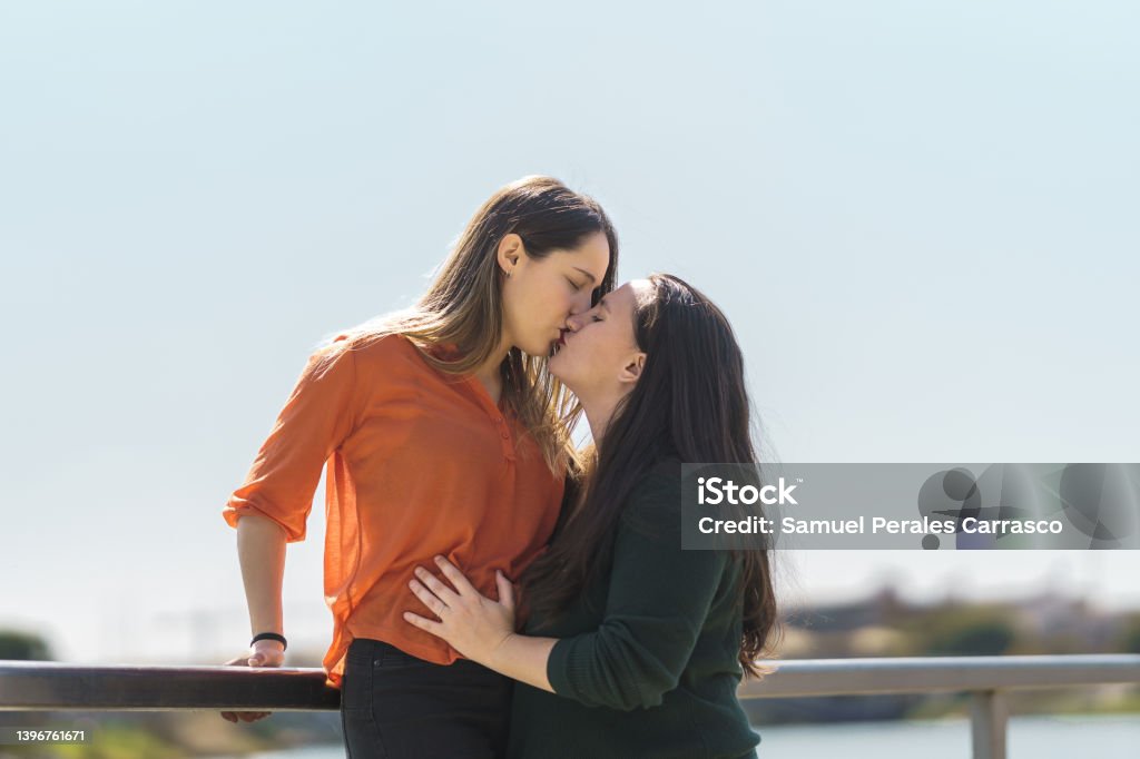 Lesbian Couple Kissing While One Of Them Is Climbing On A Railing Stock