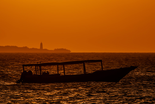 Silhouette of fishing boats anchored at sunset in the Indian Ocean, Zanzibar. Amazing landscape of pleasure boats on a background of orange sky. Golden sunset on tropical African sea. Tanzania, Africa