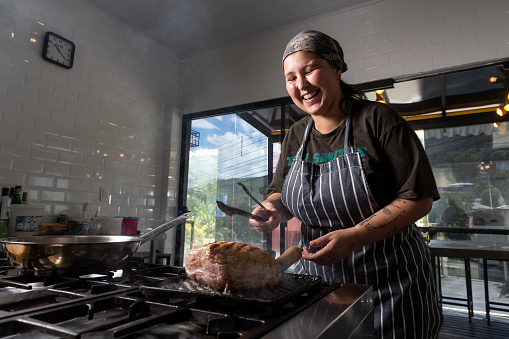 Woman kitchen chef grilling a pork shoulder