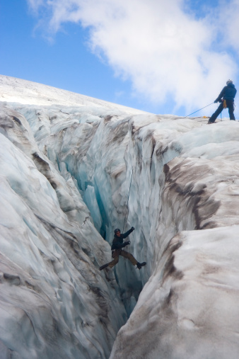 A man being z-pulleyed out of a large crevasse on a glacier at the top of a mountain.