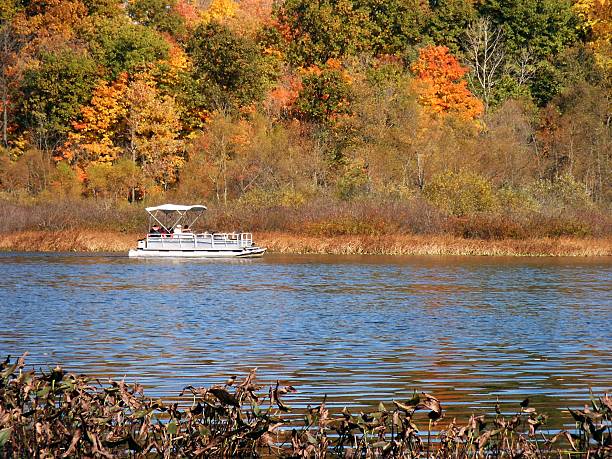 Pontoon boat across lake Pontoon boat on far shore of lake with autumn colors in background pontoon boat stock pictures, royalty-free photos & images