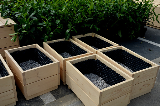 preparation for planting flower pots. wooden flower pots are filled at the bottom with gravel as drainage. the sides are covered with black foil with bubbles, prunus laurocerasus, caucasica