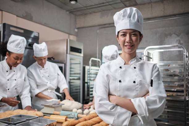 Young beautiful Asian female chef looks at camera, a cheerful smile in kitchen. stock photo