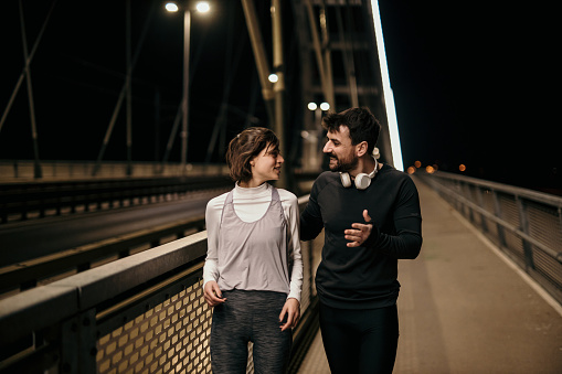 A young man and woman are walking after running outside at night across the bridge.