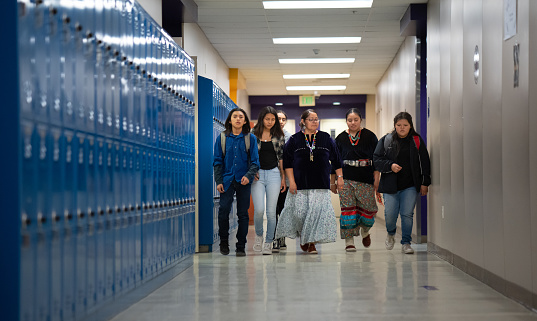 Indigenous Navajo Teacher walking among a group of middle and high school kids alongside a corridor