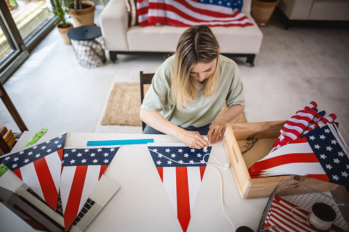 Photo of young woman making decoration for Fourth of July holiday at home.