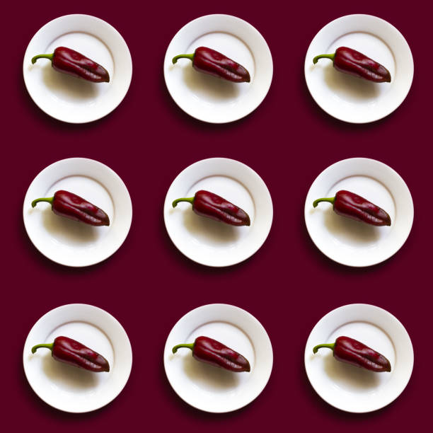 Pattern of the same Red bell pepper on the white plate on the red background. Minimalism Top view, flat lay.