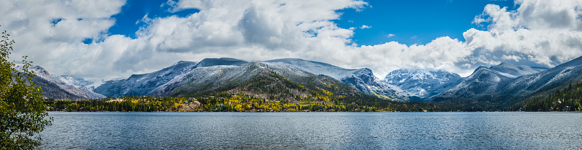 Beautiful panorama of Colorado mountain range by the lake in autumn; mountains covered with snow; small town at the base of the mountains