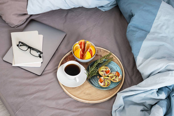 istock Coffee cup, cold tartlets and grapefruit on wooden tray, laptop, eyeglass and notebook on bedding. Breakfast in bed, cosy morning at home. 1396786817