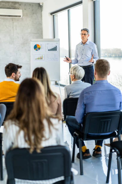 Mid adult CEO giving a business presentation to his colleagues on whiteboard in the office. stock photo