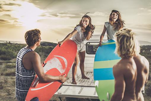 Young happy couples having fun while packing their surfboards at the back of a pick-up truck in summer day.