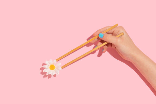 istock Spring or summer creative layout with woman hand holding chopsticks and white flowers on pastel pink background. 80s or 90s retro fashion aesthetic concept. Minimal romantic food idea. 1396791911