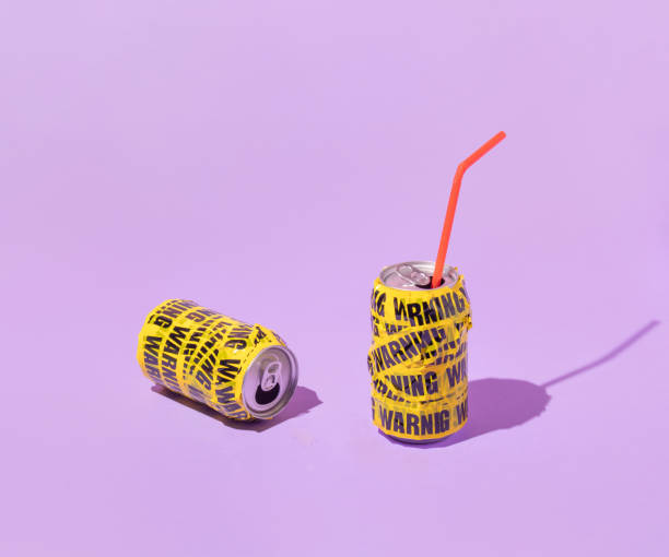 mise en page créative estivale avec des canettes de soda enveloppées dans du ruban d’emballage d’avertissement sur fond violet pastel. concept de boisson esthétique rétro des années 80 ou 90. idée d’été minimale. - pop art drink can can soda photos et images de collection