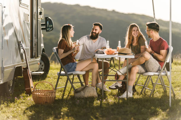 istock Young cheerful couples talking at picnic table by the camp trailer. 1396793195