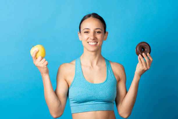 istock Hispanic sportswoman holding fruit and chocolate donut 1396795123