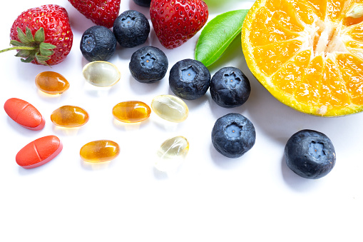 Vitamin supplement with healthy fruits blueberry, strawberry, and orange on white wood background.Top view.