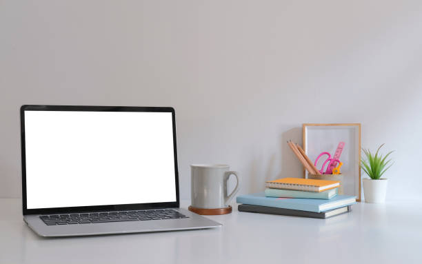 istock Mockup laptop with empty display, coffee cup, books and picture frame on white table. 1396802378